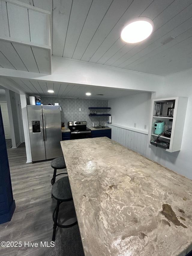 kitchen with a sink, wainscoting, wood finished floors, a breakfast bar, and appliances with stainless steel finishes