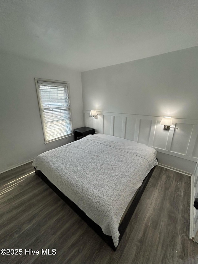 bedroom with dark wood-type flooring, a decorative wall, and a wainscoted wall
