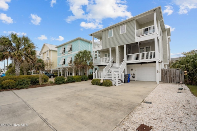 raised beach house with covered porch, concrete driveway, an attached garage, stairs, and a balcony