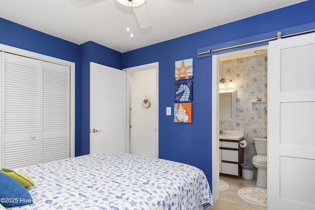 bedroom featuring a closet, ceiling fan, connected bathroom, and a barn door
