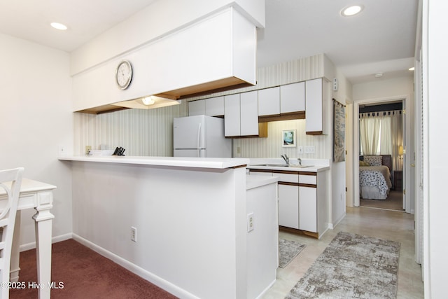 kitchen featuring freestanding refrigerator, a peninsula, white cabinets, a sink, and light countertops