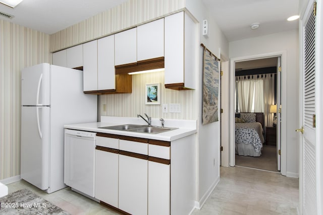 kitchen with baseboards, white appliances, light countertops, white cabinetry, and a sink