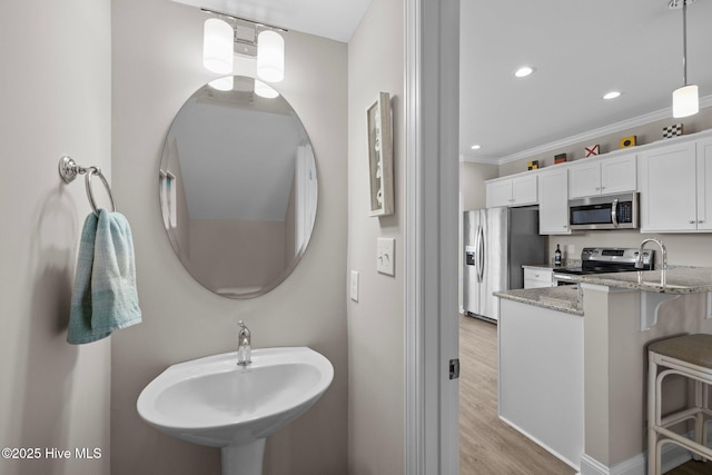 bathroom with wood finished floors, recessed lighting, ornamental molding, and a sink