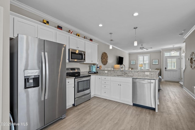 kitchen with a sink, stainless steel appliances, light wood-style floors, a peninsula, and ornamental molding