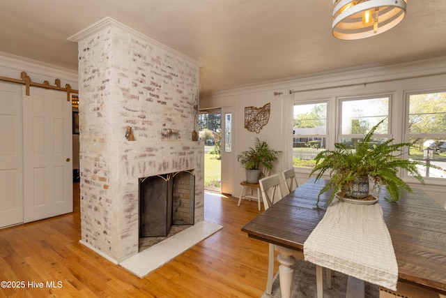 206 Robin Ln, Edenton, NC 27932 - dining room with crown molding, light wood-style flooring, a fireplace, a barn door, and healthy amount of natural light