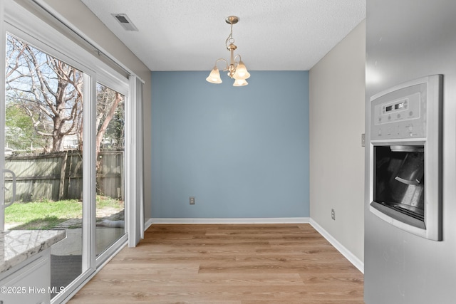 unfurnished dining area with baseboards, a textured ceiling, light wood-style floors, visible vents, and a notable chandelier