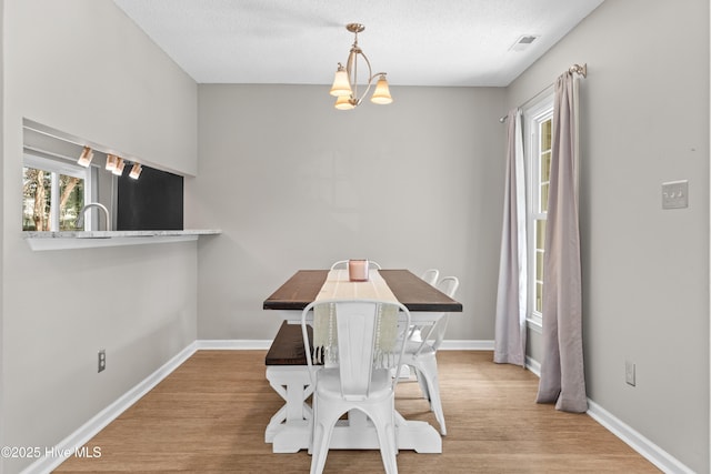 dining area with a textured ceiling, visible vents, baseboards, wood finished floors, and an inviting chandelier