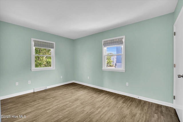 spare room featuring baseboards, visible vents, a wealth of natural light, and wood finished floors