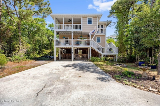 beach home featuring a porch, driveway, a ceiling fan, and stairs