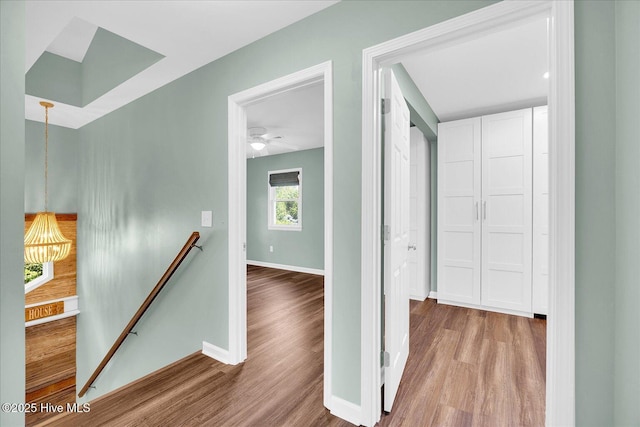 hallway featuring baseboards, an upstairs landing, and wood finished floors