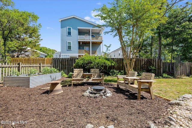 back of property featuring a fenced backyard, a fire pit, a balcony, and a garden