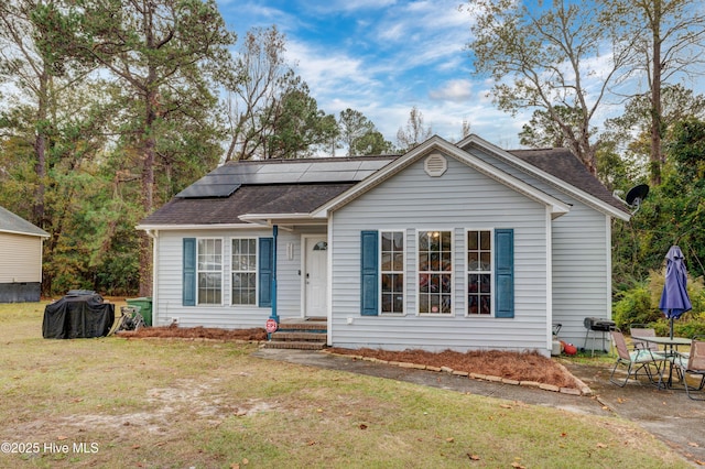 view of front of property with roof with shingles, roof mounted solar panels, and a front yard