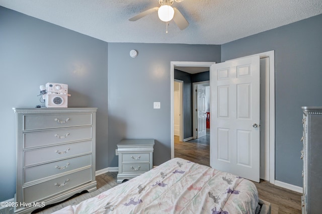 bedroom with a textured ceiling, wood finished floors, baseboards, and a ceiling fan