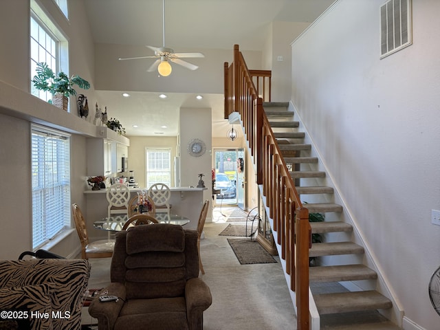 staircase with a high ceiling, ceiling fan, carpet, and visible vents