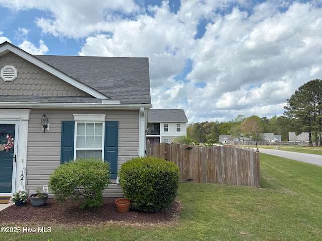 view of side of home with a yard, fence, and a shingled roof