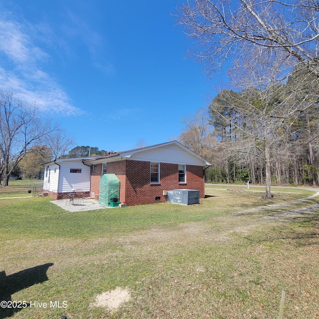 view of side of home with crawl space, a patio, brick siding, and a yard