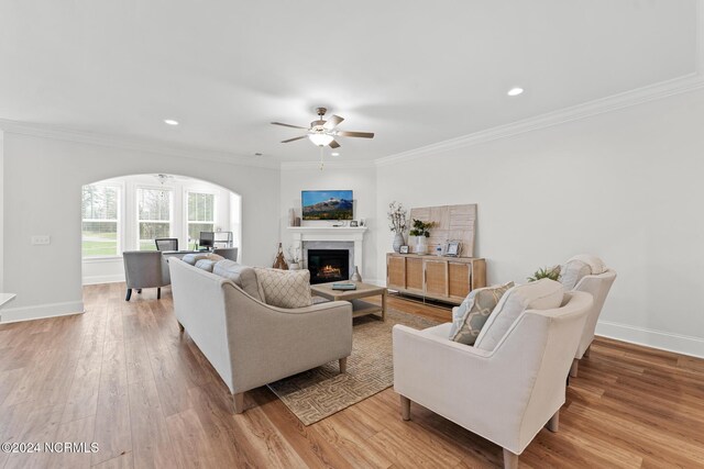 living room with crown molding, light wood-style flooring, baseboards, arched walkways, and a ceiling fan