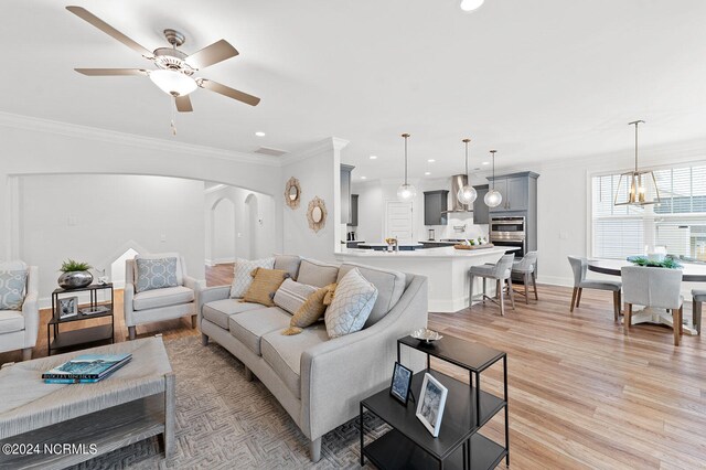 living area featuring ornamental molding, arched walkways, ceiling fan with notable chandelier, and light wood-style floors