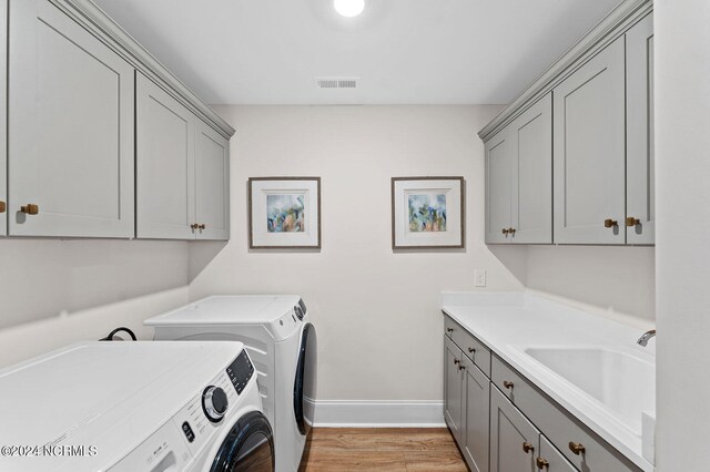 laundry room featuring washing machine and clothes dryer, light wood-style flooring, visible vents, a sink, and cabinet space