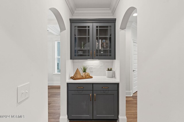 bar featuring crown molding, tasteful backsplash, wood finished floors, baseboards, and arched walkways