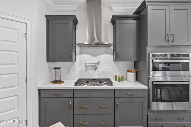 kitchen featuring wall chimney range hood, stainless steel appliances, gray cabinets, and tasteful backsplash