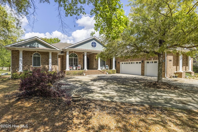 neoclassical / greek revival house with covered porch, brick siding, an attached garage, and driveway
