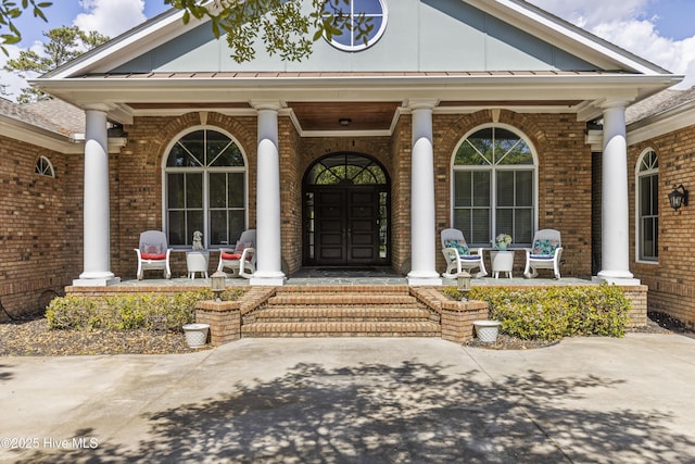 view of exterior entry featuring a standing seam roof, covered porch, and brick siding