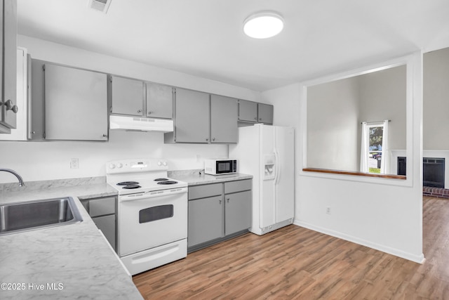 kitchen with white appliances, gray cabinetry, under cabinet range hood, light wood-style floors, and a sink