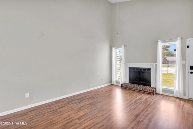 unfurnished living room with a fireplace, a towering ceiling, baseboards, and wood finished floors