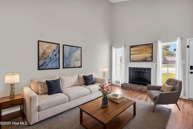 living room featuring a brick fireplace, a high ceiling, and wood finished floors