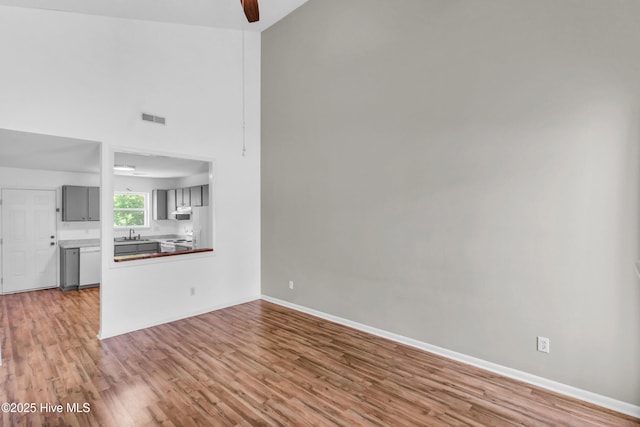 unfurnished living room with visible vents, high vaulted ceiling, a ceiling fan, and wood finished floors