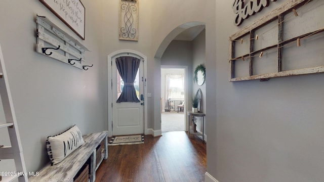 foyer entrance with dark wood finished floors, baseboards, and arched walkways
