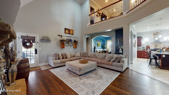 living area featuring ornamental molding, arched walkways, dark wood-style floors, and baseboards