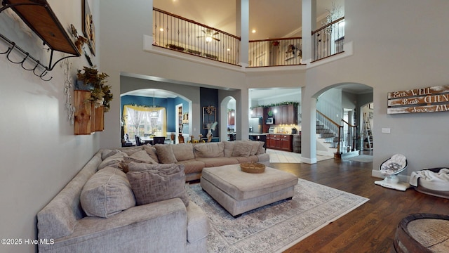 living area with arched walkways, baseboards, stairway, and wood finished floors