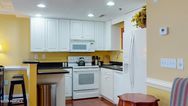 kitchen with visible vents, dark countertops, white appliances, and a sink