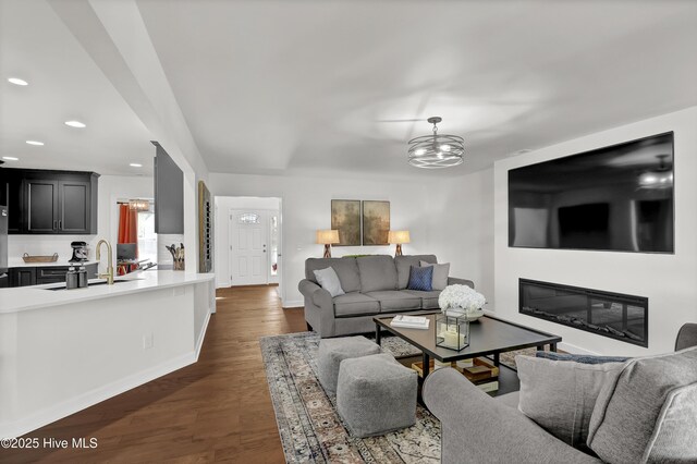 living room with a glass covered fireplace, recessed lighting, baseboards, dark wood-style floors, and a notable chandelier