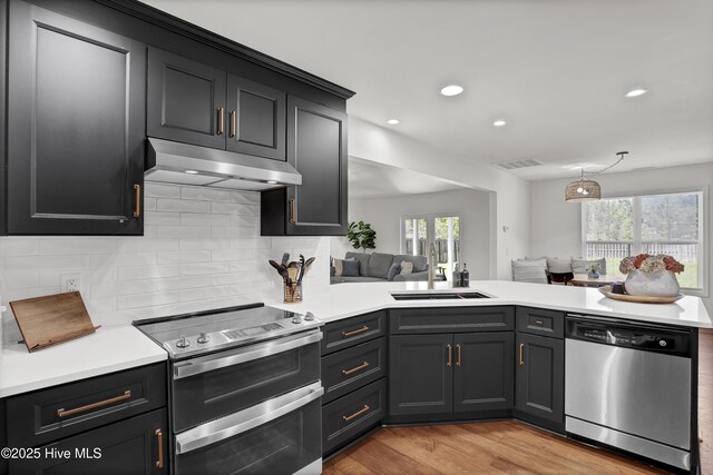 kitchen featuring light countertops, under cabinet range hood, a sink, and stainless steel appliances