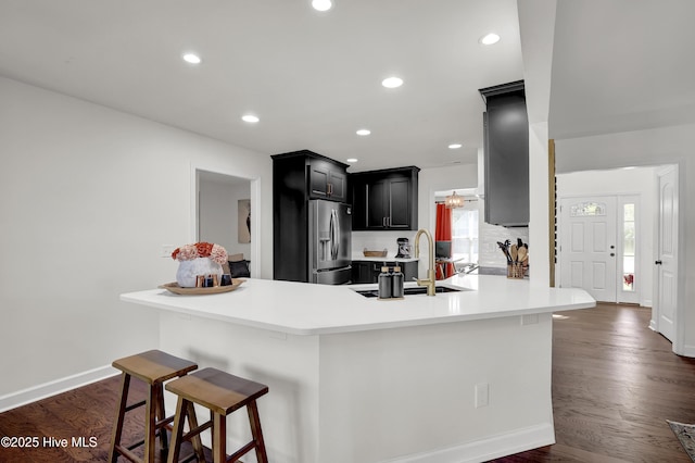 kitchen with dark wood finished floors, dark cabinets, a breakfast bar, stainless steel refrigerator with ice dispenser, and a sink