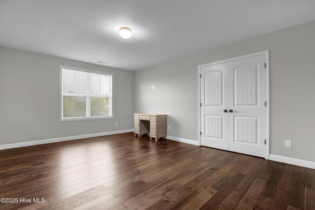 unfurnished bedroom with a closet, baseboards, visible vents, and dark wood-style floors