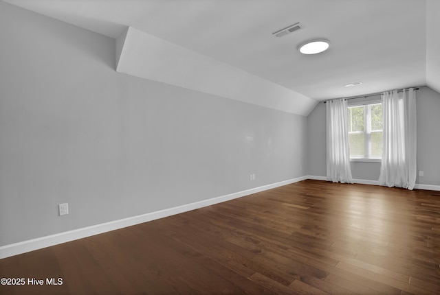 additional living space featuring visible vents, dark wood-style flooring, baseboards, and vaulted ceiling