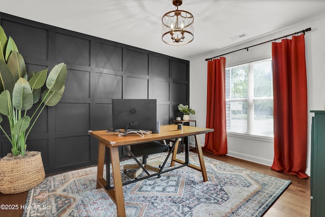 office area with a decorative wall, visible vents, a notable chandelier, and light wood-style floors