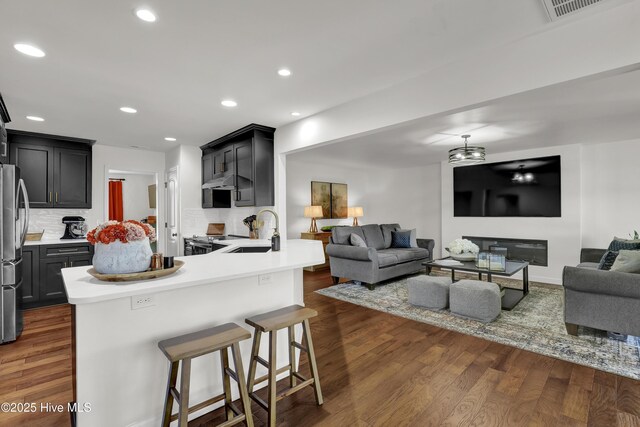kitchen with a peninsula, visible vents, a sink, open floor plan, and dark wood-style floors