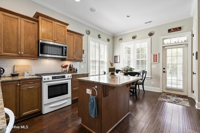 1502 Crows Landing Cir, Wilmington, NC 28403 - kitchen featuring white range with electric stovetop, stainless steel microwave, brown cabinets, dark wood-style floors, and ornamental molding