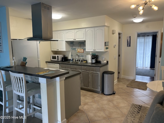 kitchen featuring dark countertops, a sink, island range hood, a breakfast bar area, and white microwave