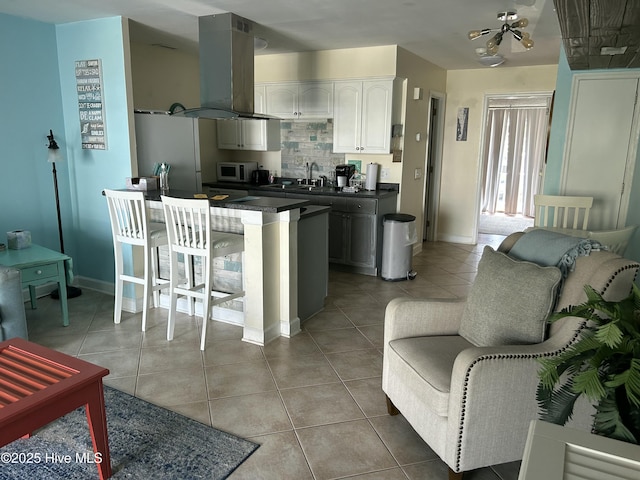 kitchen featuring dark countertops, island range hood, light tile patterned floors, white microwave, and white cabinetry