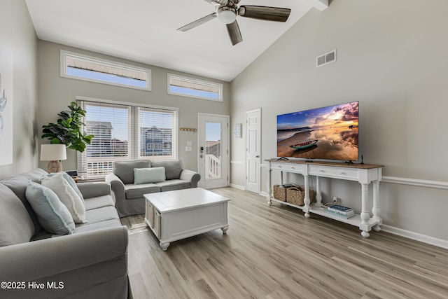 living room with visible vents, baseboards, a ceiling fan, light wood-style flooring, and high vaulted ceiling