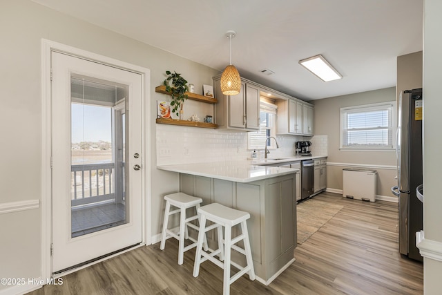 kitchen with a sink, a peninsula, light wood finished floors, stainless steel appliances, and backsplash