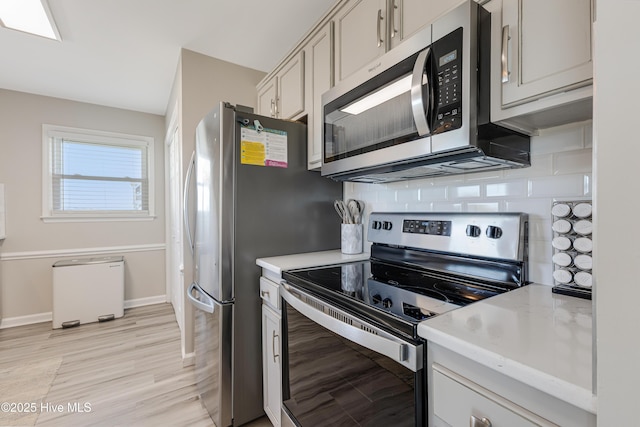 kitchen featuring light wood-type flooring, appliances with stainless steel finishes, light countertops, decorative backsplash, and baseboards