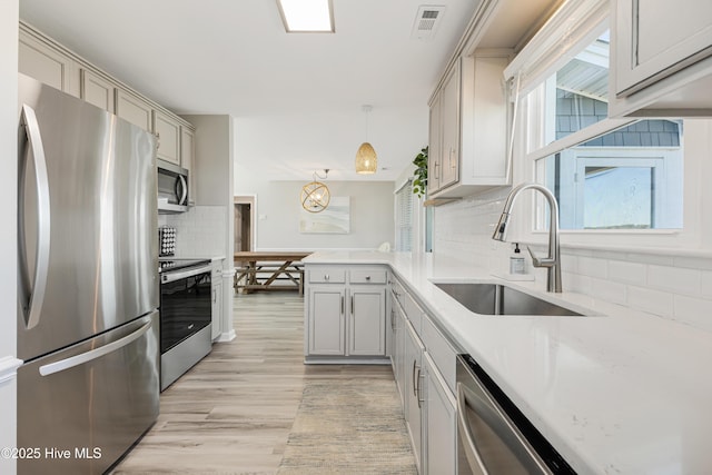 kitchen with appliances with stainless steel finishes, a peninsula, decorative backsplash, light wood finished floors, and a sink