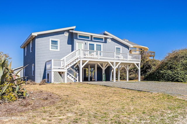 rear view of property with a carport, stairs, gravel driveway, and a lawn